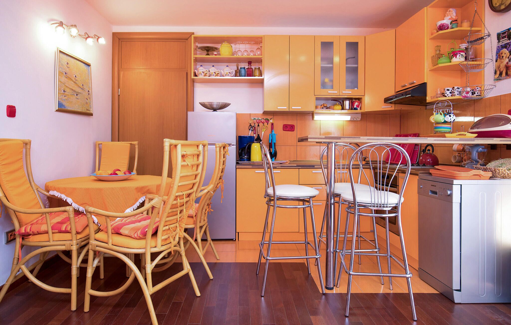 Une cuisine compacte avec des meubles en bois, un coin repas avec des chaises en osier et un petit îlot avec des tabourets.