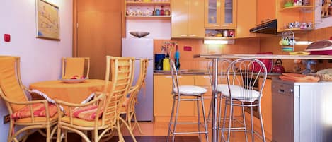 A compact kitchen with wooden cabinets, a dining area with wicker chairs, and a small island with stools.