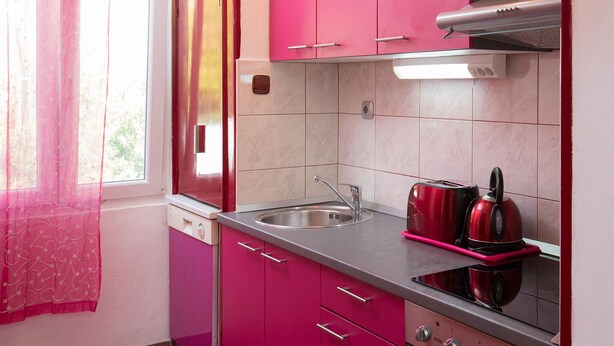 Ett kök med rosa skåp, en diskho i rostfritt stål och en röd vattenkokare.