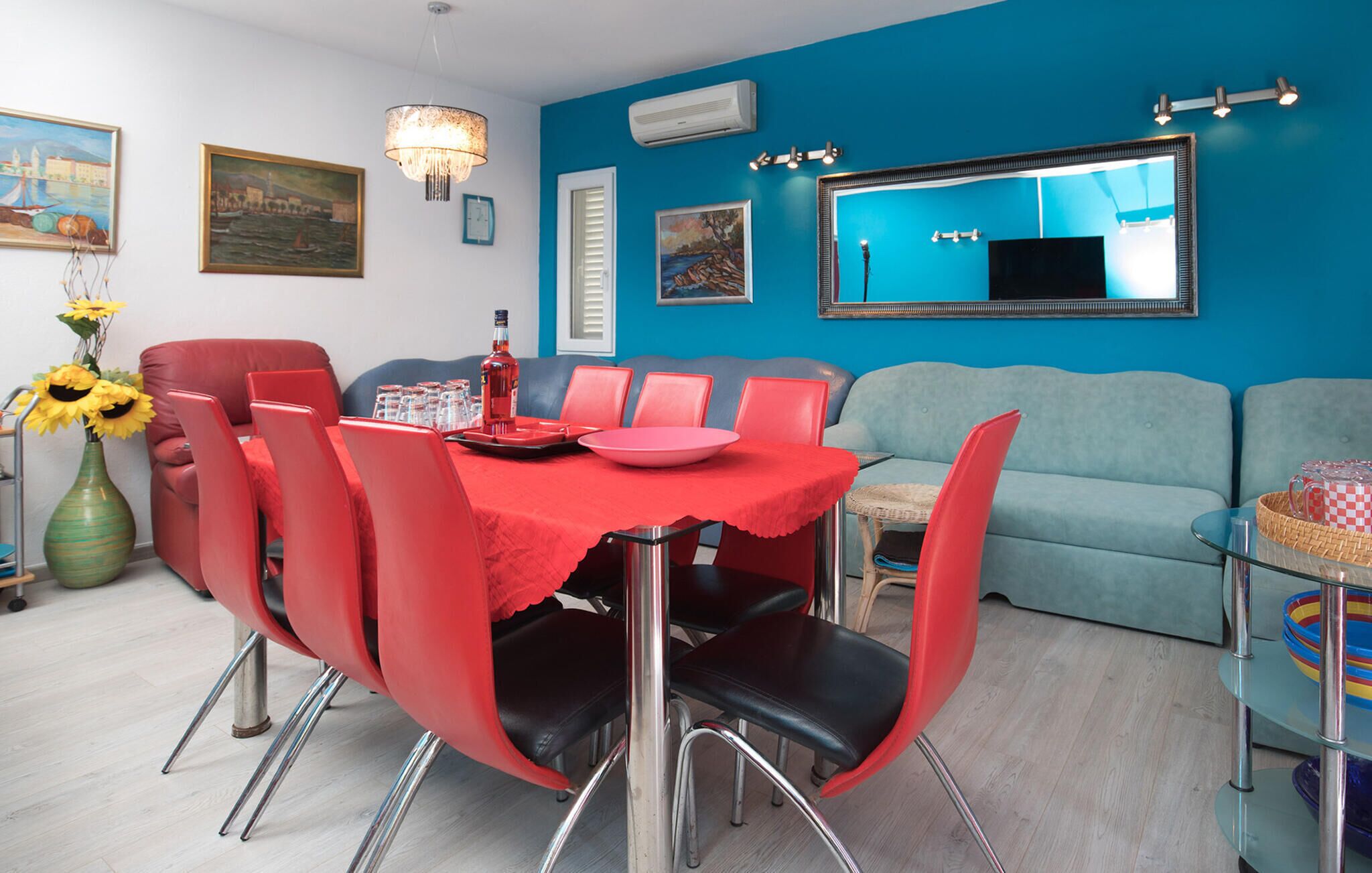 A dining area with a red tablecloth, red chairs, and a vase of sunflowers.