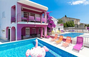 A hotel with a pool area, including a pink elephant float, lounge chairs, and a balcony with purple flowers. - Lovely apartment in Seget Vranjica with WiFi (Seget Vranjica)