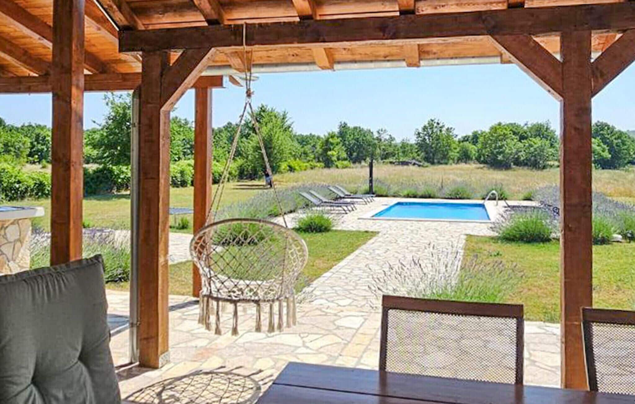 A covered outdoor area with a stone patio, a pool, and lounge chairs.