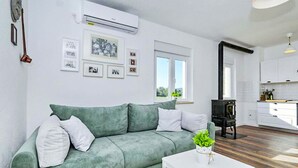 A living room with a green sofa, white cushions, a white coffee table with a plant, and a kitchen area with white cabinets and a black stove. - Pet friendly home in Ervenik (Ervenik)