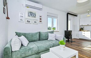 A living room with a green sofa, white cushions, a white coffee table with a plant, and a kitchen area with white cabinets and a black stove. - Pet friendly home in Ervenik (Ervenik)