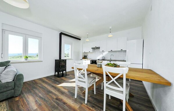 A modern kitchen with white cabinets, a wooden countertop, and a dining area with white chairs. - Pet friendly home in Ervenik (Ervenik)