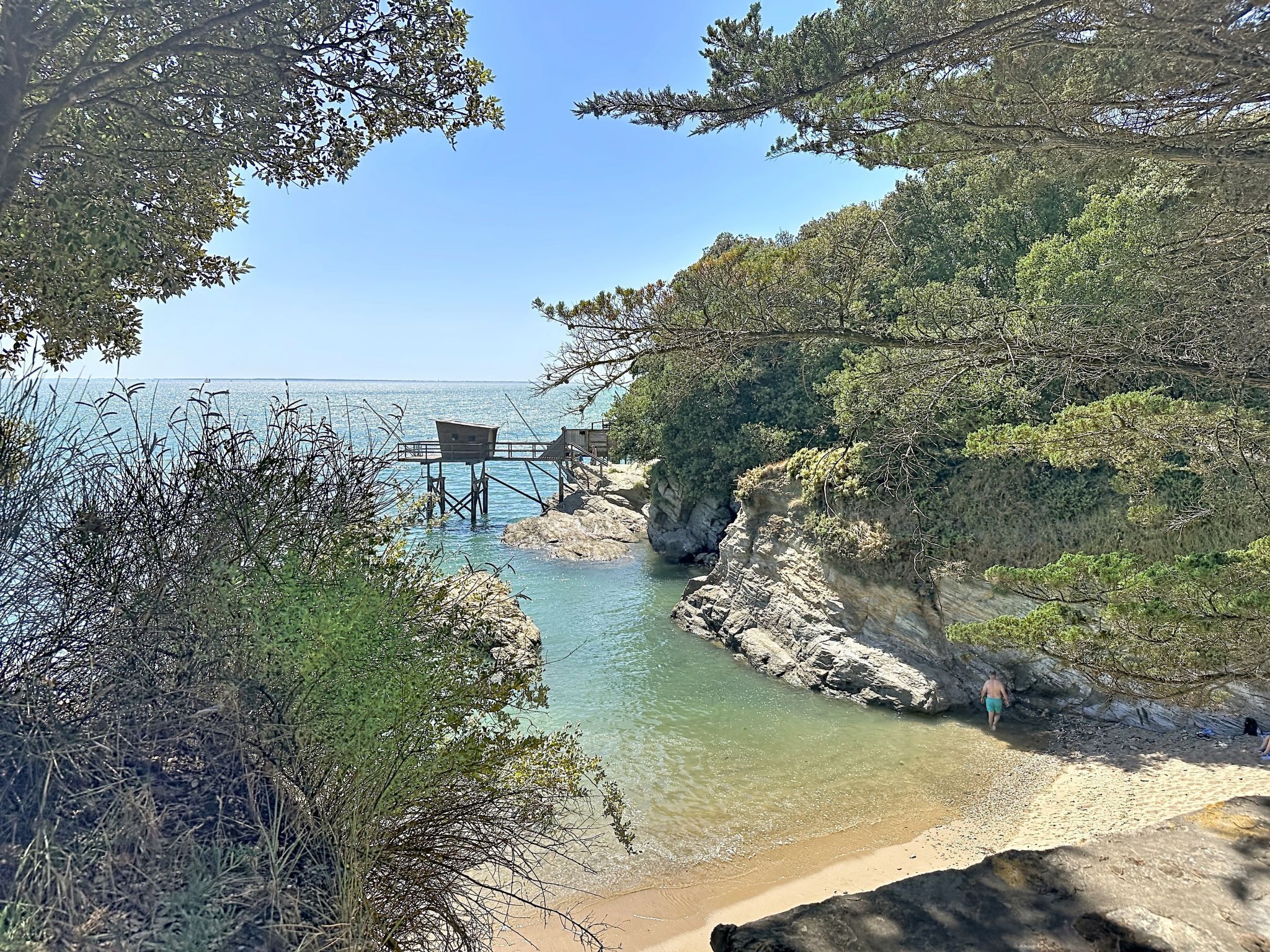 A coastal landscape with a rocky shoreline, clear water, and a wooden viewing platform.