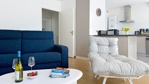 A modern living room with a blue sofa, a white armchair, and a small table with a bottle and glasses. - Les Sylphes by Interhome (Pornic)