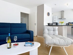 A modern living room with a blue sofa, a white armchair, and a small table with a bottle and glasses. - Les Sylphes by Interhome (Pornic)