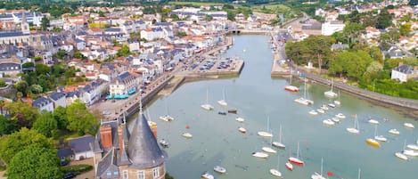 Un pueblo costero con una torre destacada, un puerto deportivo con numerosas embarcaciones y una combinación de edificios residenciales y comerciales a lo largo del paseo marítimo.