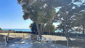 A swimming pool with a view of the sea, surrounded by a fenced patio area with chairs and a wooden fence. - Les Sylphes by Interhome (Pornic)