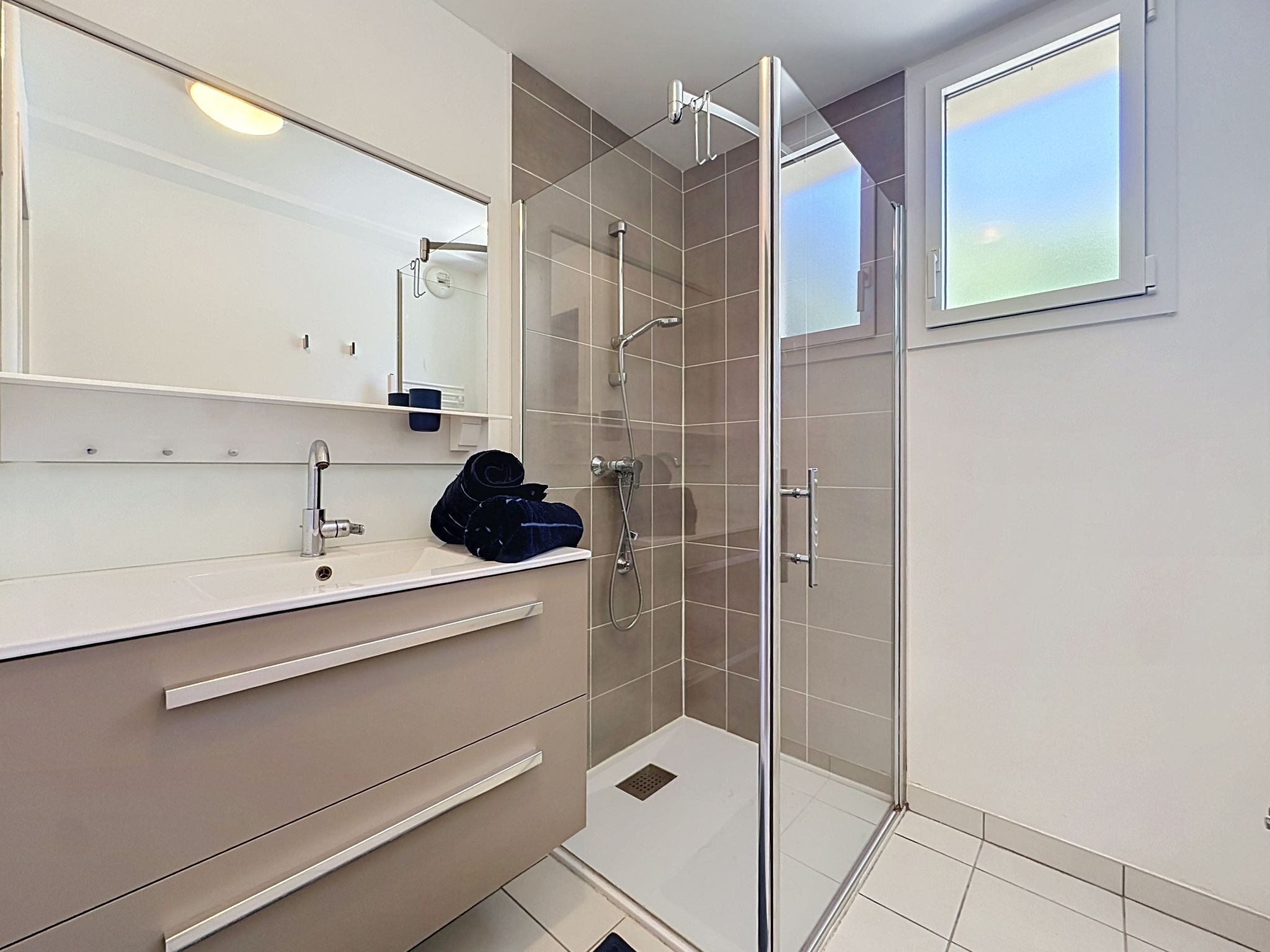 A modern bathroom with a glass shower enclosure, a white sink, and a mirror above the vanity.