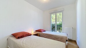 A small, bright room with two beds, a window, and a radiator. - Les Sylphes by Interhome (Pornic)