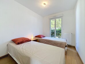 A small, bright room with two beds, a window, and a radiator. - Les Sylphes by Interhome (Pornic)