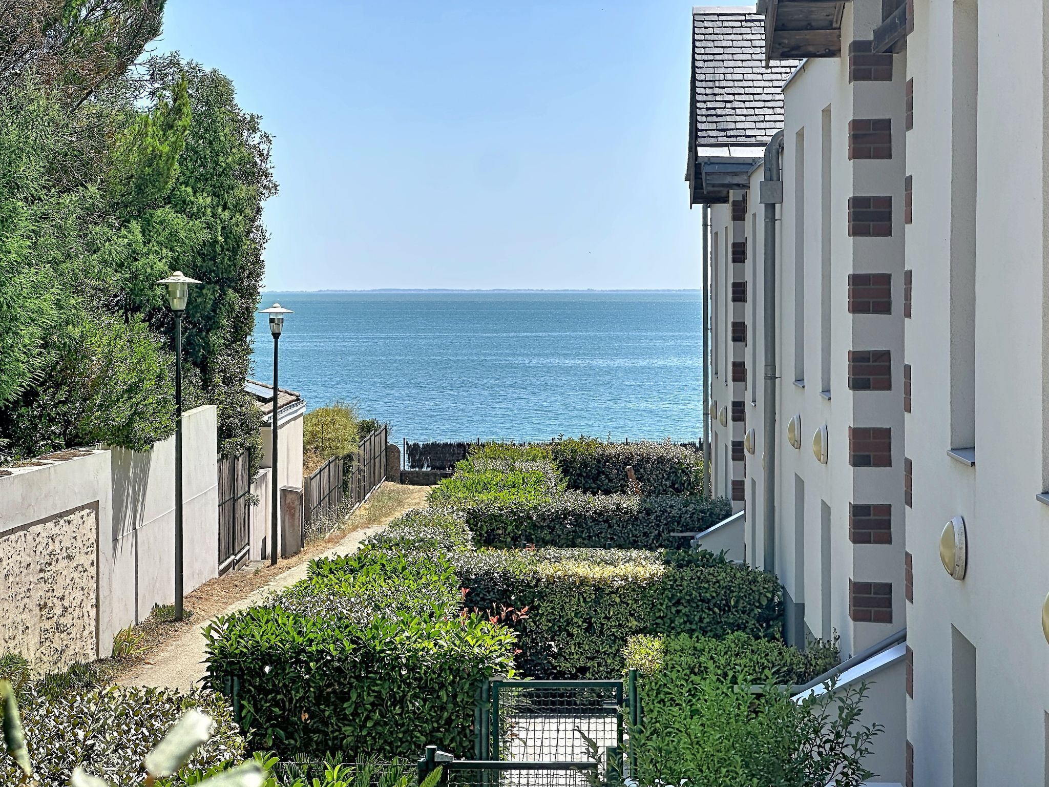 A residential area with a view of the sea, a pathway, and a building with multiple windows.