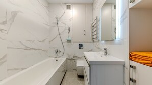 A modern bathroom with a marble wall, a bathtub, a sink, and a towel rack.