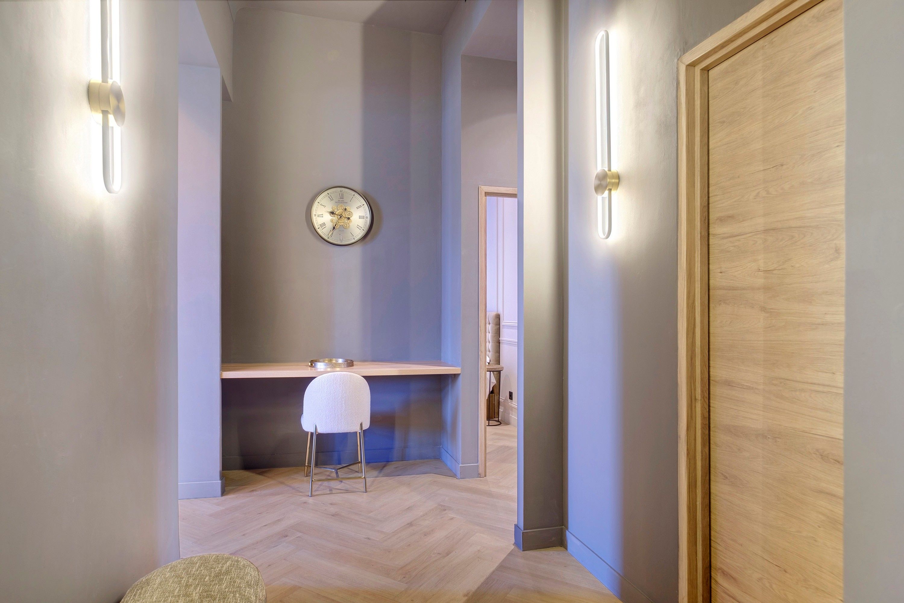 A hallway with a wooden door, a wall-mounted clock, a small stool, and a bench.