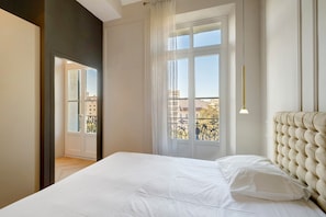 Ein Schlafzimmer mit einem großen Bett, einem Fenster mit Vorhängen und Blick auf Gebäude.