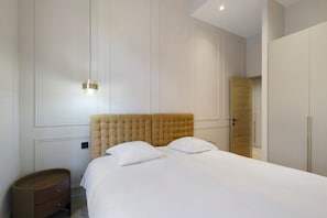 Ein Schlafzimmer mit einem großen Bett, einem Nachttisch, einem Kleiderschrank und einer Lampe.