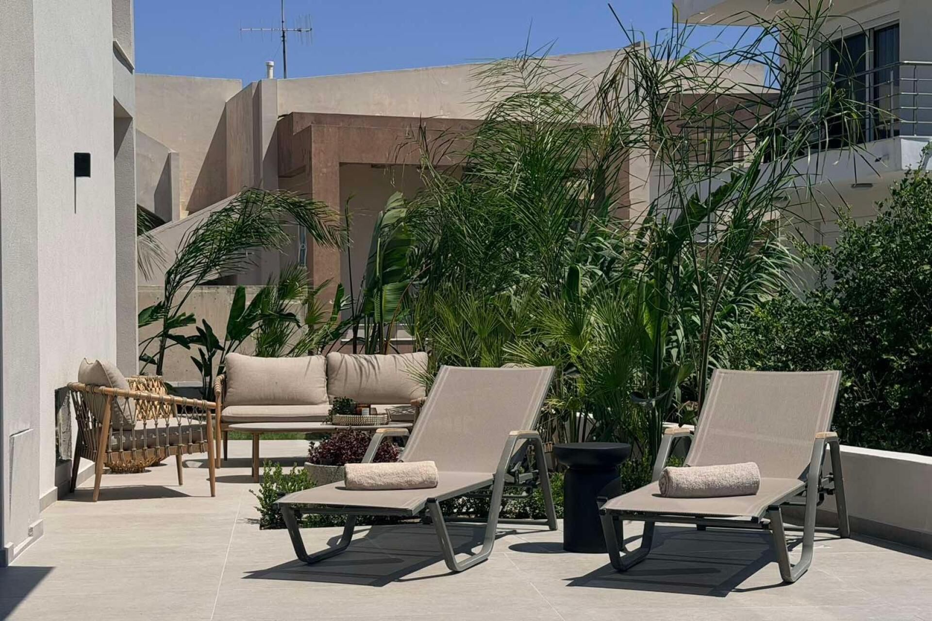 A rooftop terrace with two lounge chairs, a wicker chair, and a potted plant.