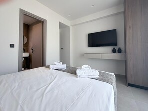 Ein modernes Hotelzimmer mit einem großen Bett, einem flachbildfernseher an der Wand und einer kleinen Sitzecke mit Handtüchern.