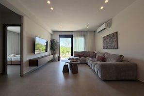 A modern living room with a large flat-screen TV, a sectional sofa, a coffee table, and a potted plant. - Mirena Exclusive Apartment 1 (Rhodes)