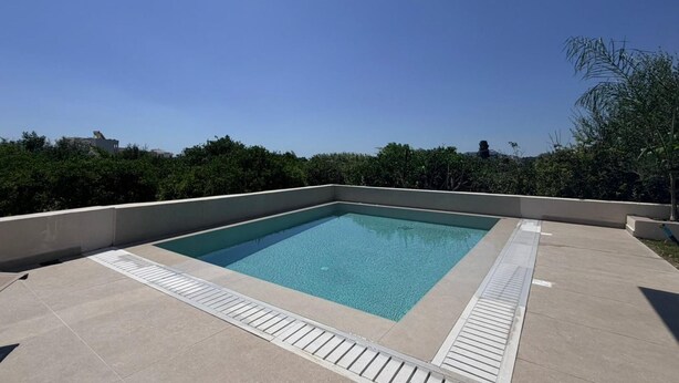 Ein rechteckiger Pool im Freien mit einer gefliesten Liegefläche und einem Metall-Geländer.