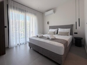 A modern bedroom with a large bed, a small bedside table, and a view through sheer curtains. - Mirena Exclusive Apartment 1 (Rhodes)