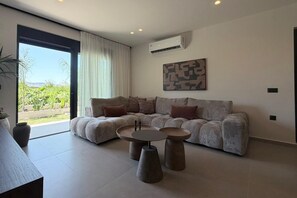 Ein modernes Wohnzimmer mit einem grauen Sofa, zwei runden Couchtischen und einem großen Fenster mit Vorhängen.