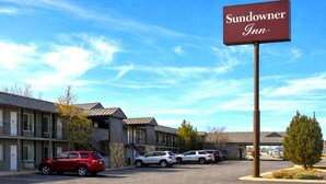A Sundowner Inn with a clear sky, a parking lot with several cars, and a building with a stone facade. - 2 Queen Beds Non-Smoking (Forsyth MT)