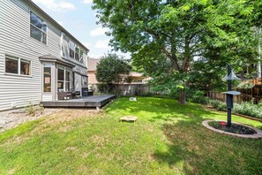 A residential backyard with a wooden deck, a lawn, and a large tree.