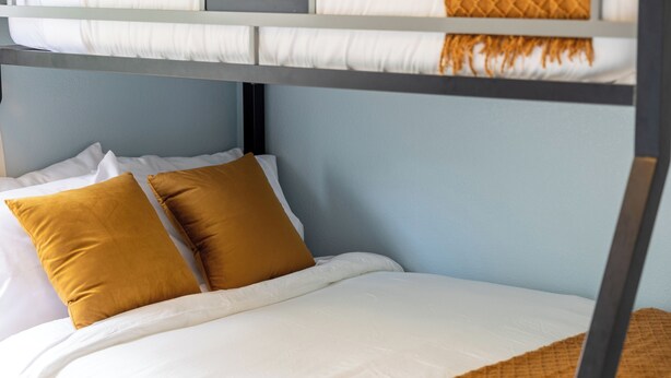 A bunk bed with white bedding and two mustard-colored pillows.