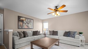 A living room with a sofa set, a coffee table, a ceiling fan, and a painting on the wall.
