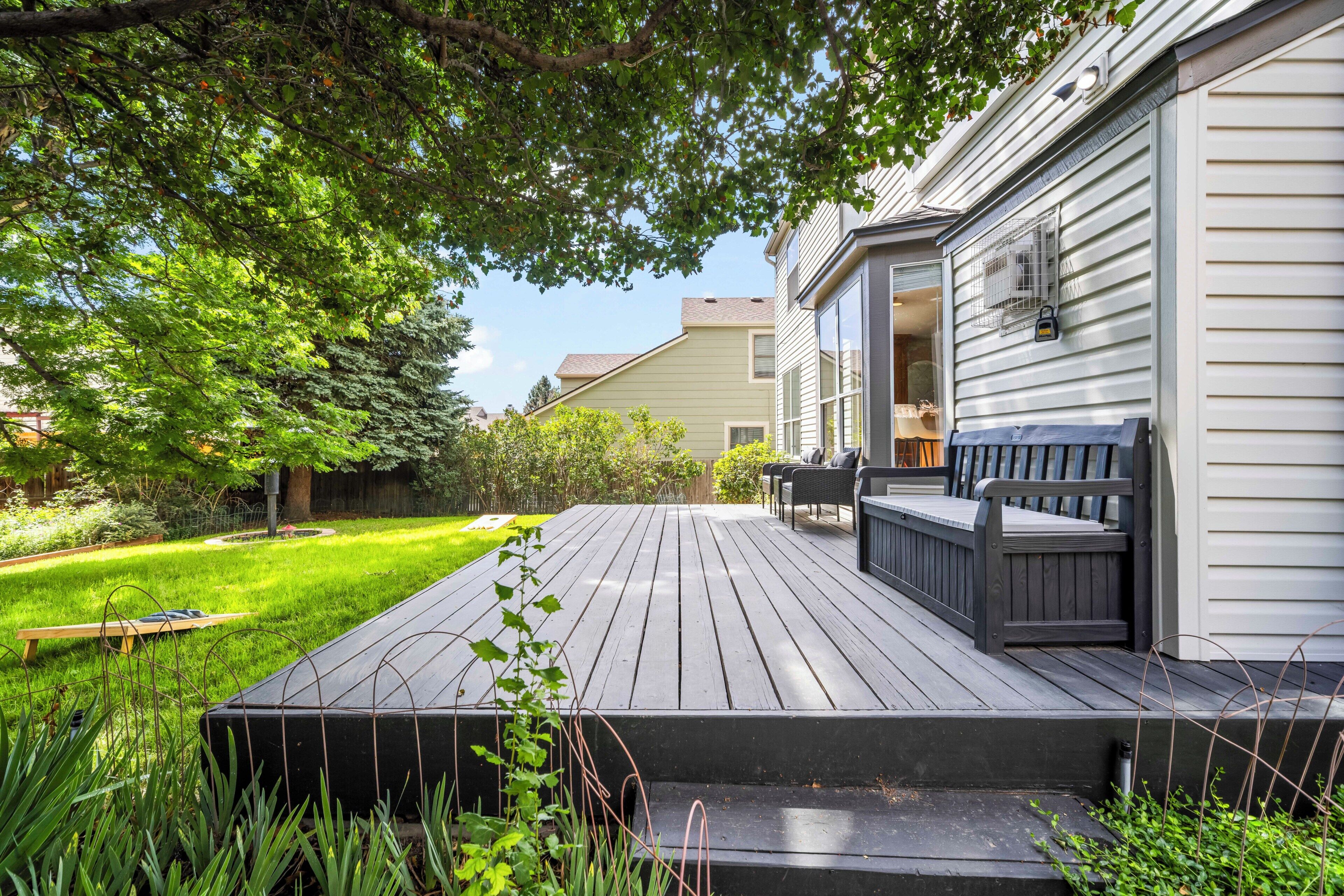 Une terrasse avec coin salon extérieur, une pelouse et une maison avec un revêtement extérieur et des fenêtres.