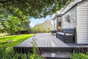 A deck with outdoor seating, a grassy yard, and a house with siding and windows.