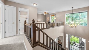 A multi-level interior with a staircase, a ceiling fan, and a window with a view of greenery.