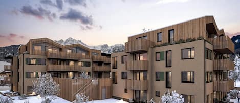 Een modern meerlaags gebouw met balkons en grote ramen, omgeven door met sneeuw bedekte bomen en bergen.
