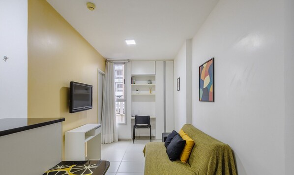 Um espaço de estar compacto com cozinha compacta, um sofá com almofadas, uma cadeira, uma televisão e um quadro na parede.