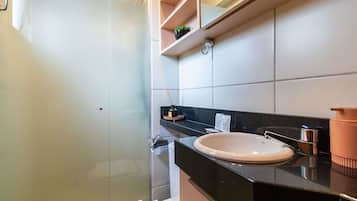 Un baño moderno con cabina de ducha de vidrio, encimera negra y lavamanos blanco.