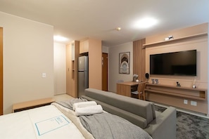 Una habitación de hotel con cama, sofá, escritorio, televisión y refrigerador.