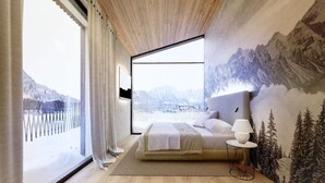 Ein Schlafzimmer mit großem Fenster, einem Bett, einem Nachttisch und einer Wandmalerei von einer Berglandschaft.