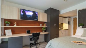 A modern bedroom with a bed, a desk with a laptop, a TV, and a kitchenette. - Student Only The Lyra (London)