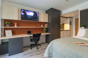 Ein modernes Schlafzimmer mit einem Bett, einem Schreibtisch mit Laptop, einem Fernseher und einer Küchenzeile.