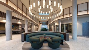 A spacious lobby with a curved seating area, a central coffee table, and a staircase leading to upper floors. - Student Only The Lyra (London)