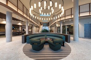 Eine großzügige Lobby mit einer gebogenen Sitzecke, einem zentralen Couchtisch und einer Treppe zu den oberen Stockwerken.