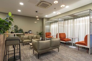 Ein moderner Lounge-Bereich mit Sofas, einer Kaffeemaschine und einer Glastrennwand.