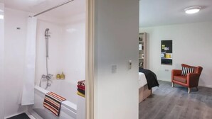 A modern bathroom with a shower, a bathtub, and a toilet. There is a small seating area with a chair and a shelf with various items. - Student Only The Lyra (London)