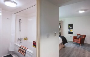 Ein modernes Badezimmer mit Dusche, Badewanne und Toilette. Eine kleine Sitzecke mit einem Sessel und einem Regal mit diversen Gegenständen.