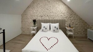 Un dormitorio con pared de piedra, una cama con adorno en forma de corazón y una mesita de noche con un jarrón de flores.