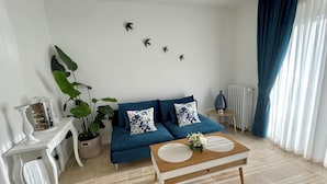 Un salón con un sofá azul, una mesa de centro, una planta en maceta y decoración en la pared.