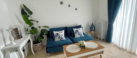 A living room with a blue sofa, a coffee table, a potted plant, and wall art.